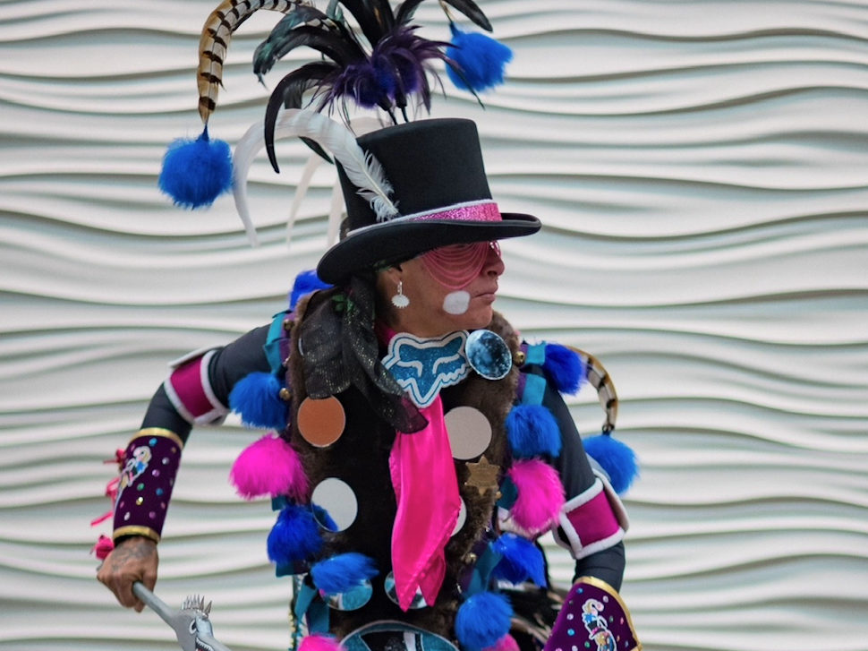 Powwow dancer Kevin Francis wears a decorated top hat and vibrant Prairie Chicken Dance regalia while posing for a portrait.